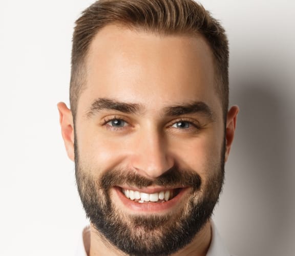 Middle aged man smiling and standing in front of a white wall