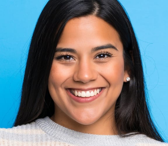 Young woman standing in front of blue wall and smiling