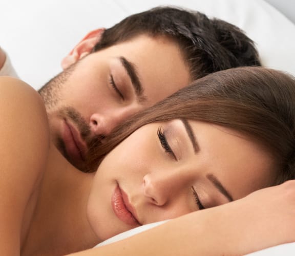 Couple cuddling in a bed with their eyes closed